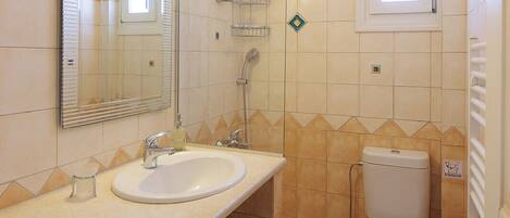 A compact bathroom with a sink, mirror, toilet, and a washing machine.