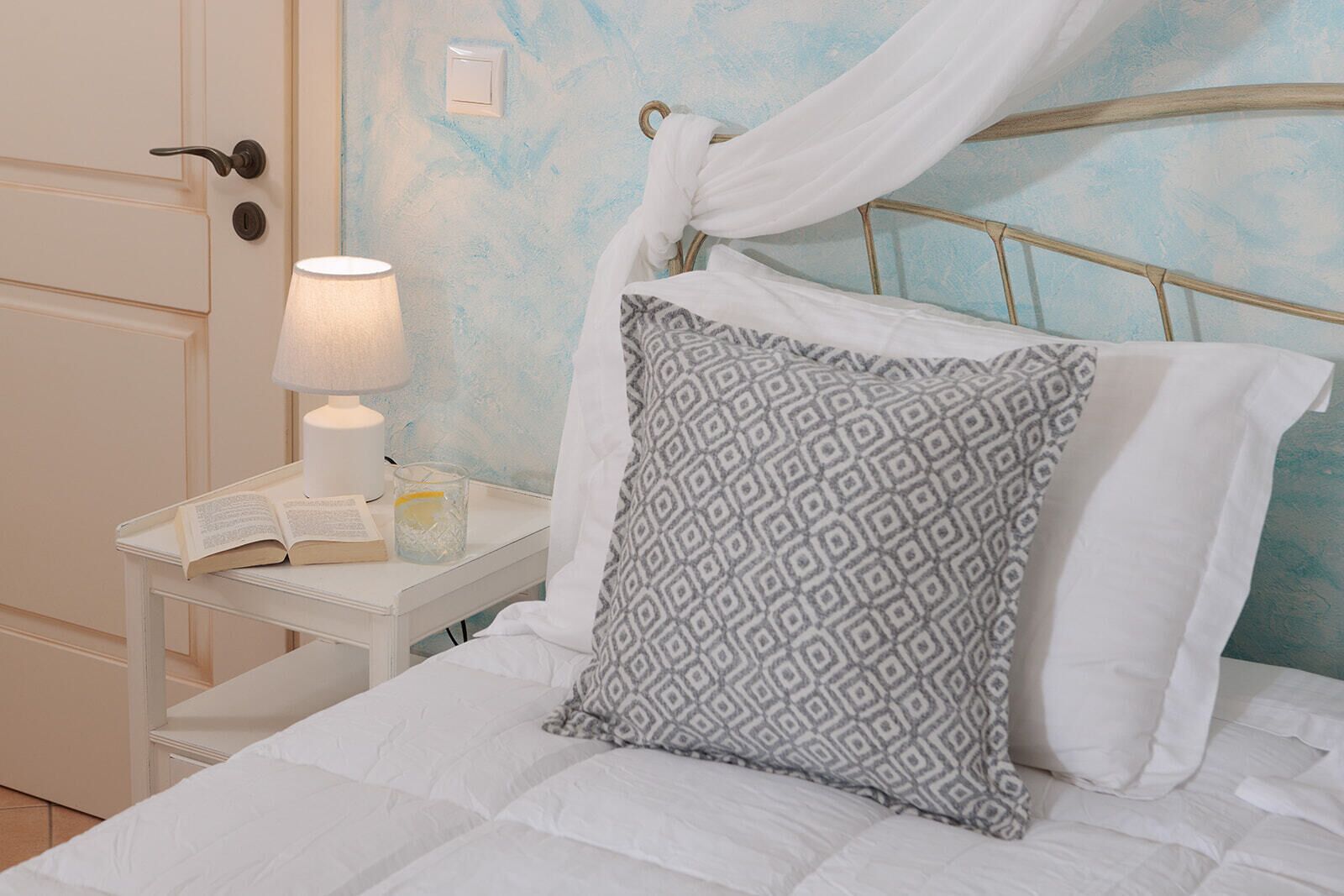 A neatly made bed with a patterned pillow, a bedside lamp, and an open book on a nightstand.