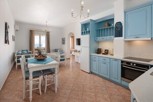 Una cocina moderna con armarios azules, un comedor con mesa y sillas, y vista al mar a través de una ventana.