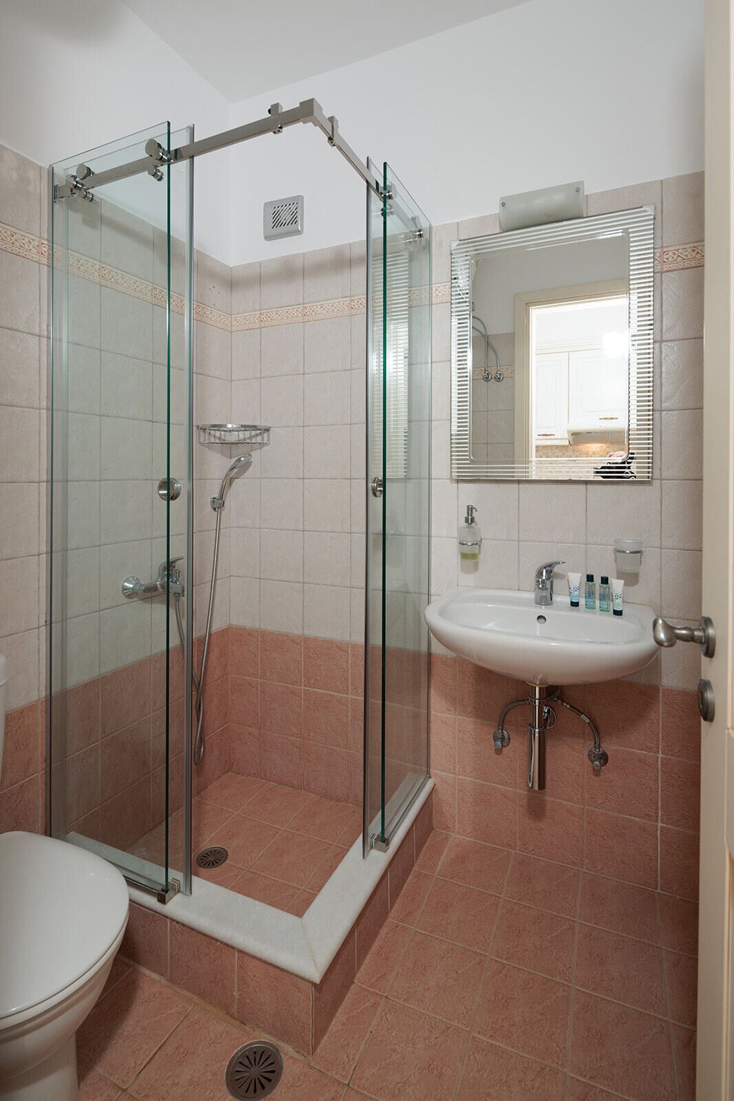 Une salle de bain avec une douche à parois de verre, un lavabo blanc avec des articles de toilette et un miroir au-dessus du lavabo.