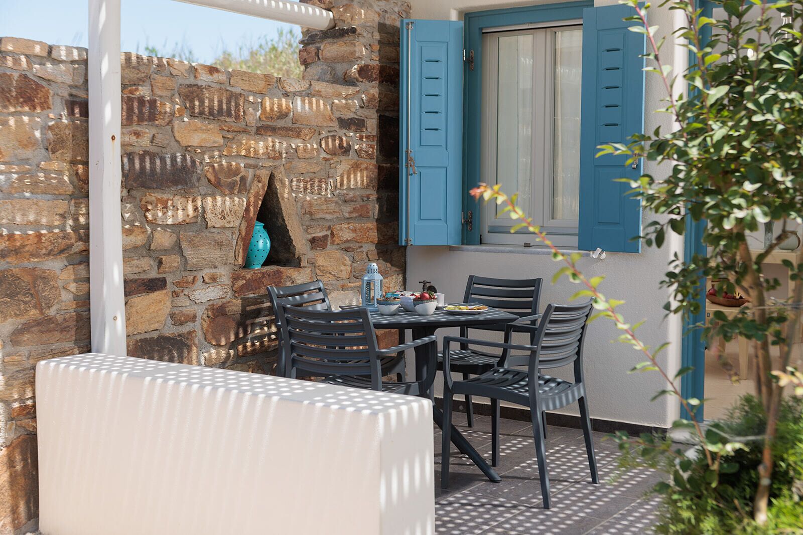 A stone wall with a window, a table with chairs, and a blue door.