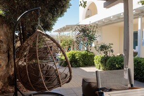 A wicker hanging chair, a cushioned outdoor seating area, and a building with a white facade and arched windows. - 9 Muses Naxos beach hotel (Naxos)