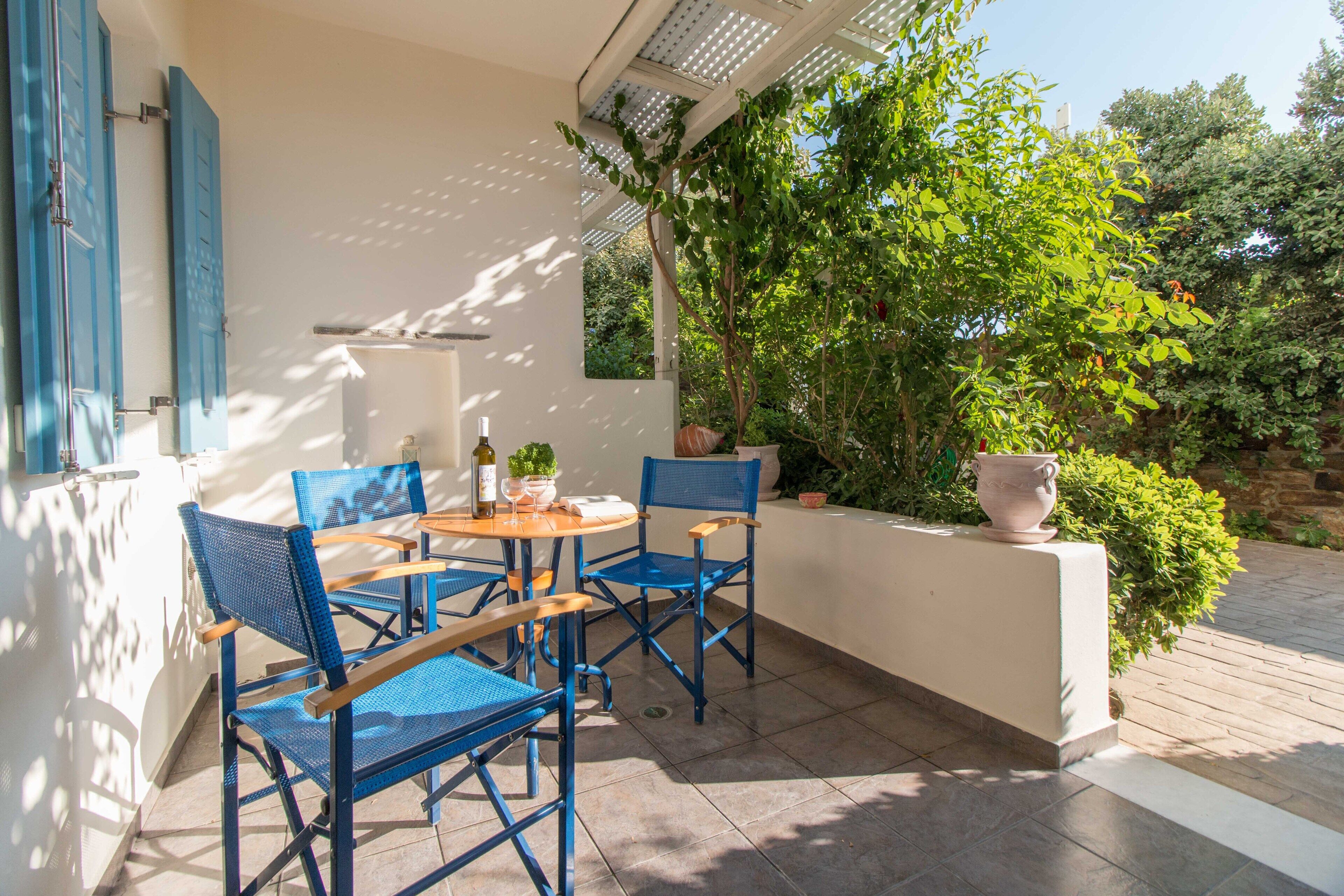 An outdoor patio with a table and chairs, a potted plant, and a view of greenery.