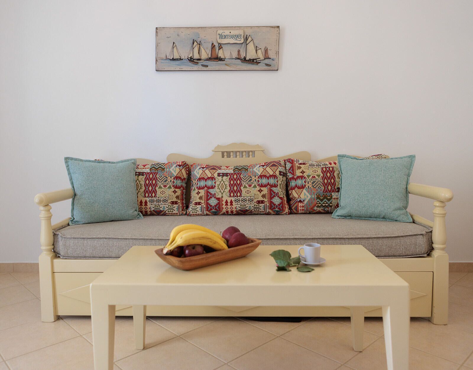 A cozy living room with a sofa, pillows, a coffee table, and a painting of sailboats.