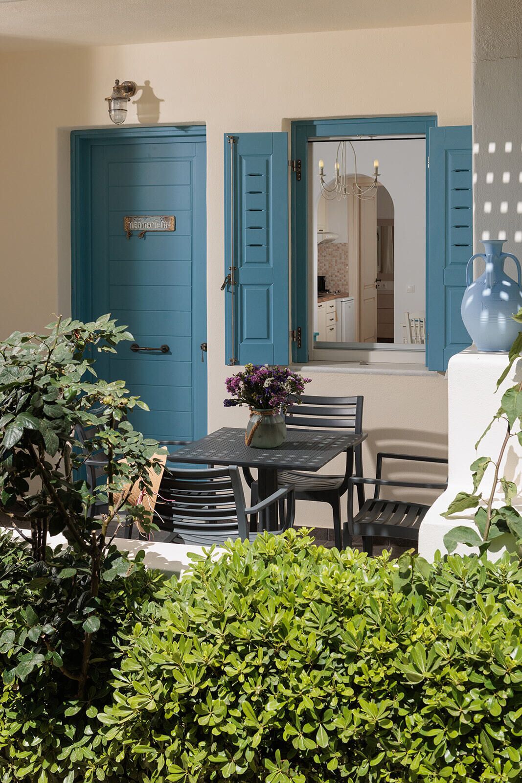 A dining area with a table and chairs, a blue door, and a window with a view into a kitchen.