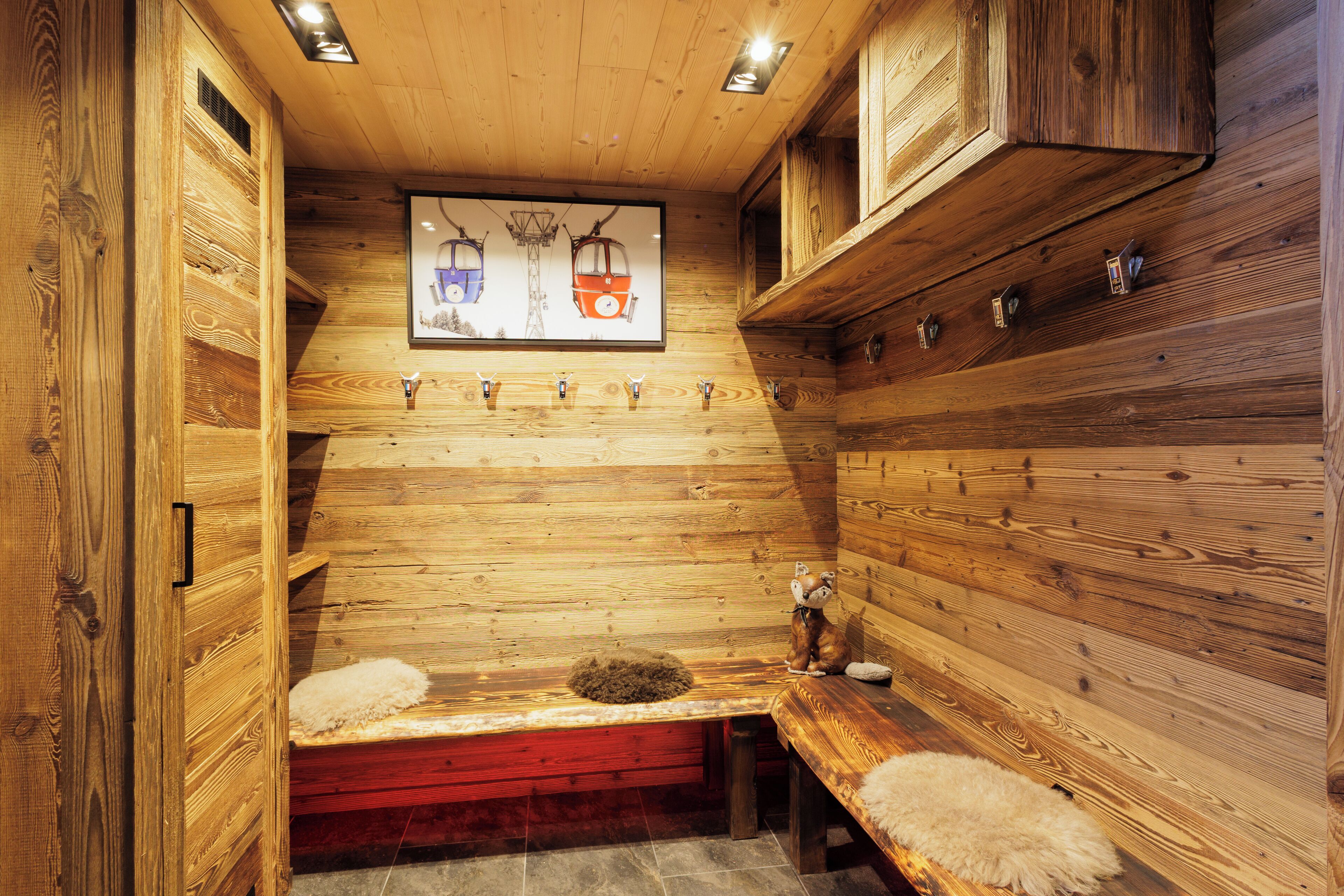 Eine Holzsauna mit Bänken, eine Bank mit einem flauschigen Teppich und ein an der Wand hängendes Bild von Seilbahnen.