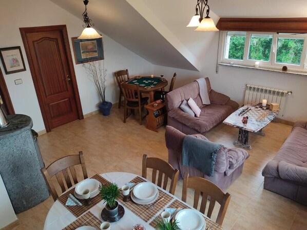 Un salon chaleureux comprenant un coin repas, une cheminée et une fenêtre donnant sur un paysage verdoyant.