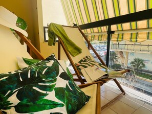 A room with a window view of a parking lot, a chair with a green towel, and a pillow with a leaf pattern.