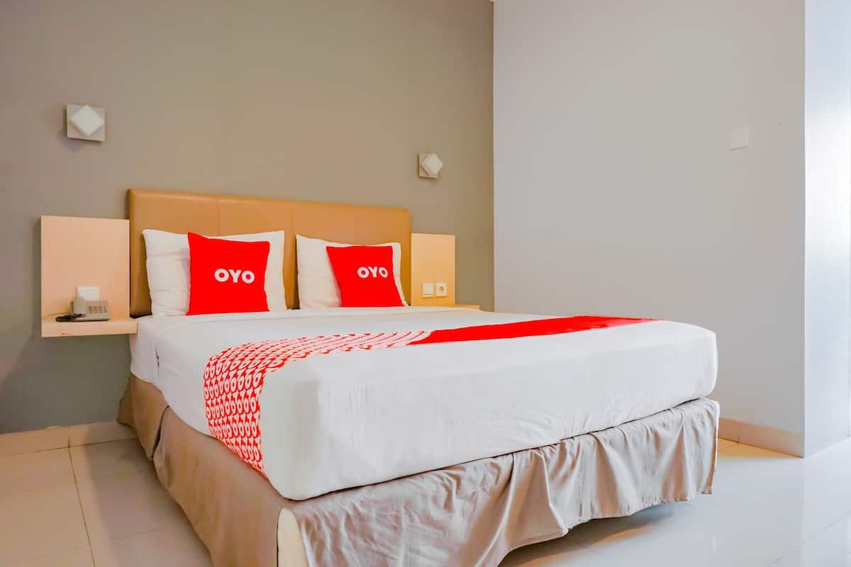 Cama bem arrumada com edredom branco e vermelho, duas almofadas vermelhas com a palavra "OYO" estampada e duas luminárias de mesa.