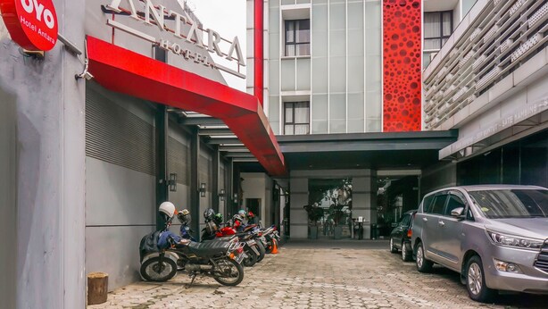 L’entrée d’un hôtel, avec un auvent rouge, une enseigne indiquant « Hôtel Antara », ainsi que plusieurs motos et voitures garées.