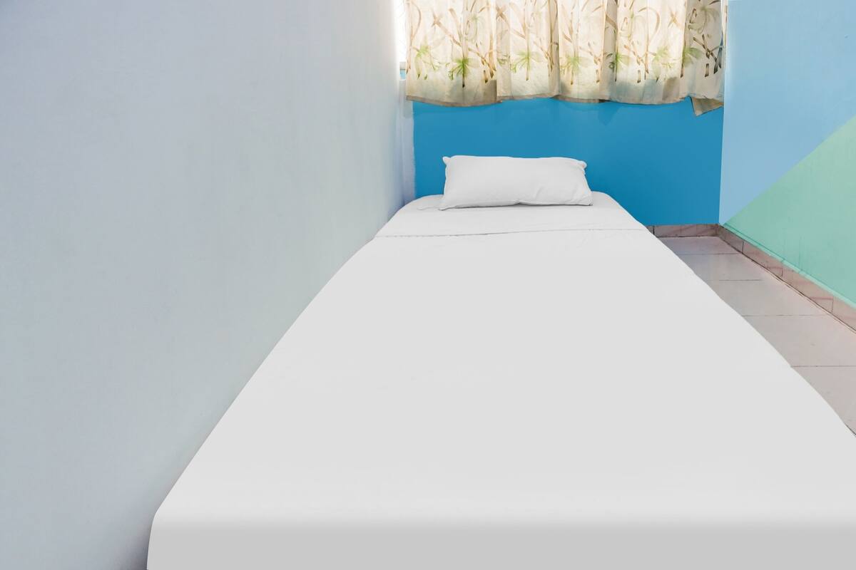 A single bed with a white mattress and pillow in a room with blue and light blue walls.