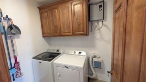 Une buanderie équipée d’un lave-linge et d’un sèche-linge, de meubles de rangement en bois, d’un radiateur mural et d’un aspirateur.