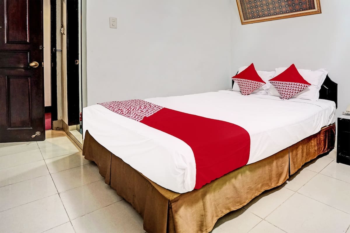 Un lit bien fait, recouvert d’une couette blanche et rouge, avec un couvre-lit marron et deux oreillers à motifs rouges et blancs.