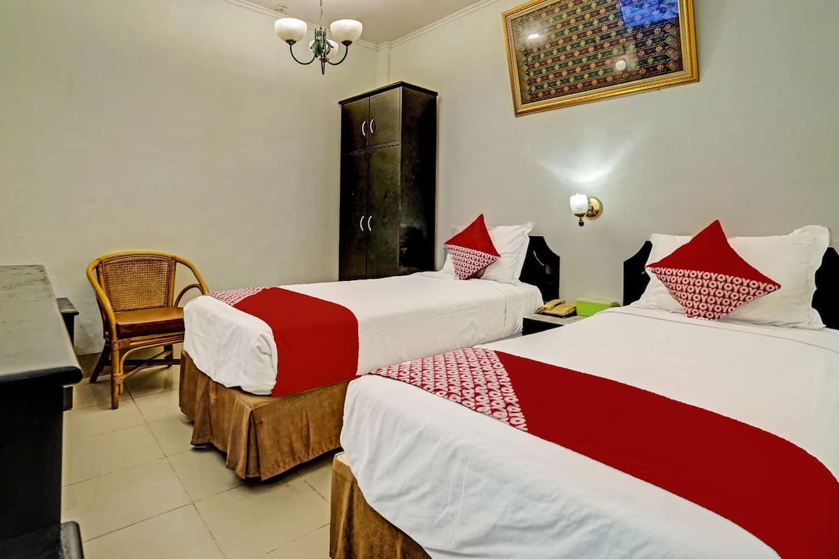 Une chambre d’hôtel avec deux lits, une armoire, une chaise, un bureau et un lustre.