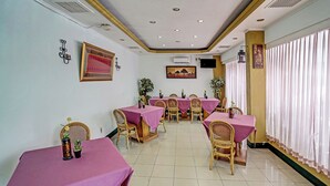Comedor con mesas cubiertas de manteles rosas, sillas de mimbre y plantas en macetas.