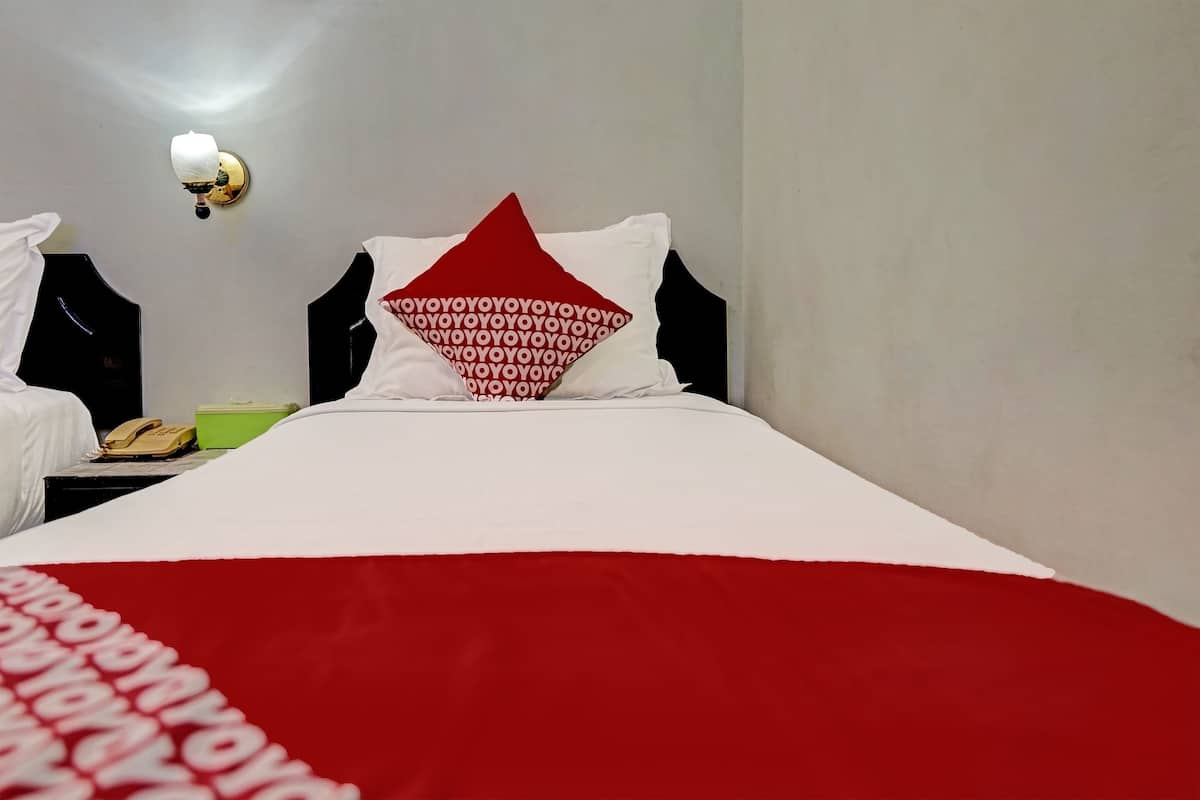 Une chambre d’hôtel avec un lit bien fait, un téléphone sur la table de chevet et un luminaire fixé au mur.