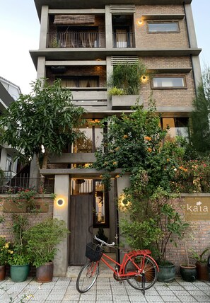 A modern multi-story building with balconies, potted plants, and a bicycle parked in front. - Kaia Gallery Hotel (Da Nang)
