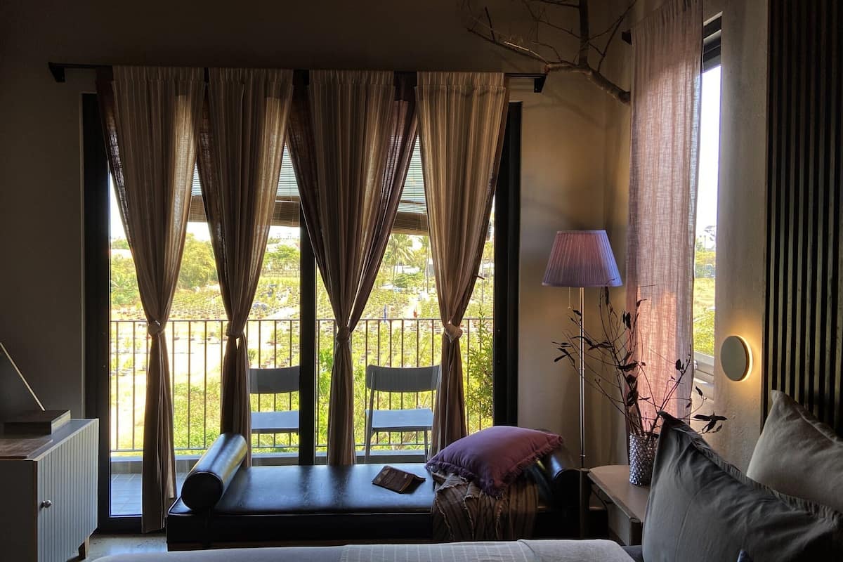 A bedroom with a bed, a bedside table with a lamp, a window with curtains, and a view of the outside.