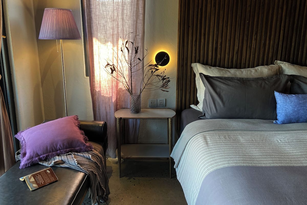 A hotel room with a bed, bedside table, lamp, and a wall-mounted light fixture.