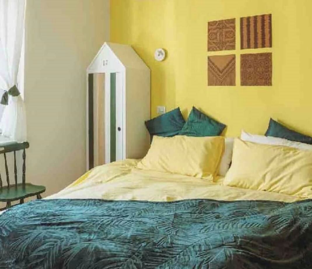 Een bed met een beddekleed met patroon, een wit hoofdbord en meerdere kussens.