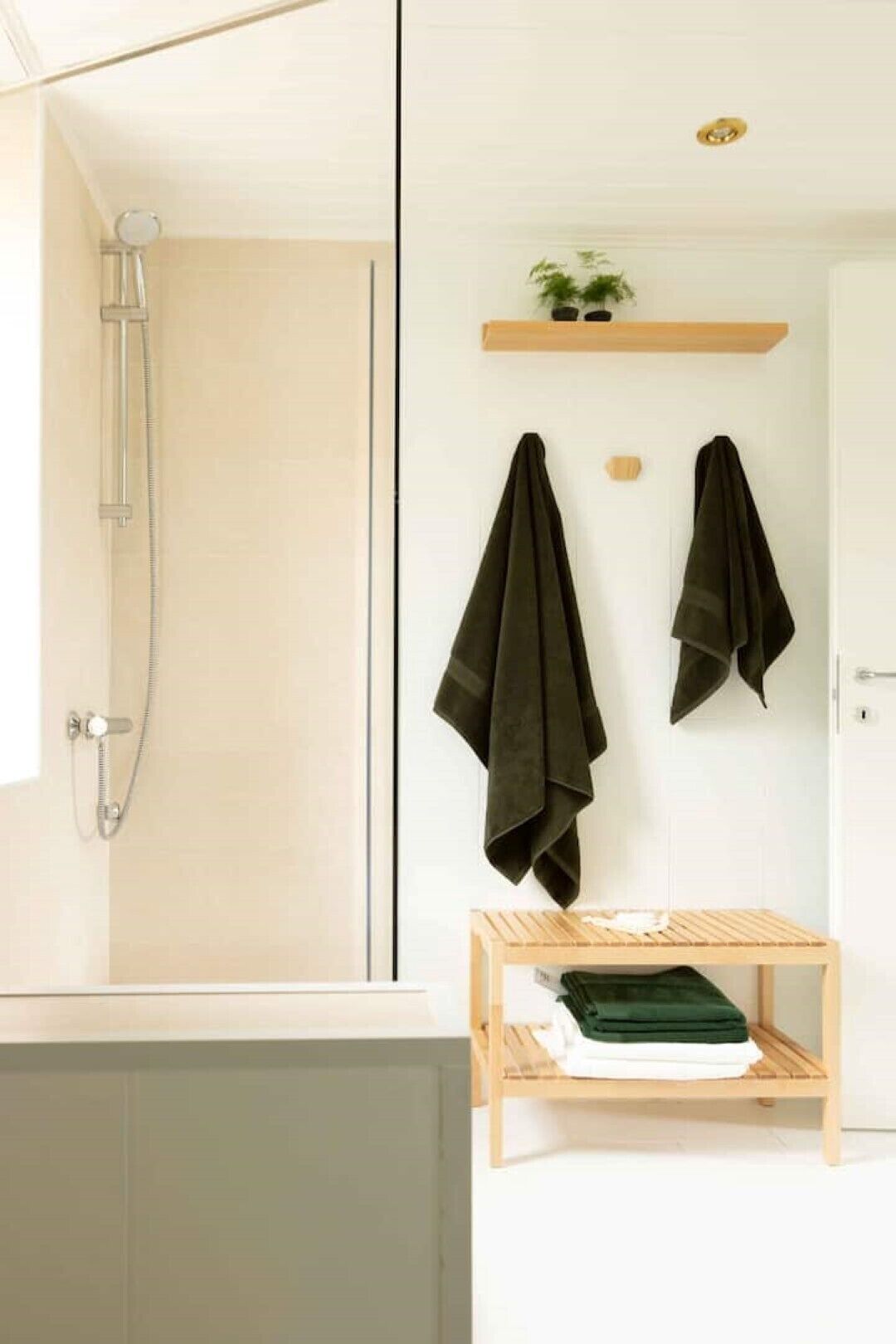 Un baño con ducha, perchero y repisa con toallas dobladas.
