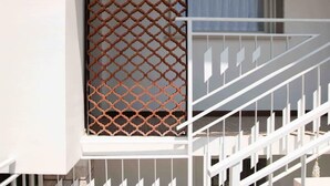 Una escalera blanca con barandilla de metal que conduce a un ventanal con celosía.