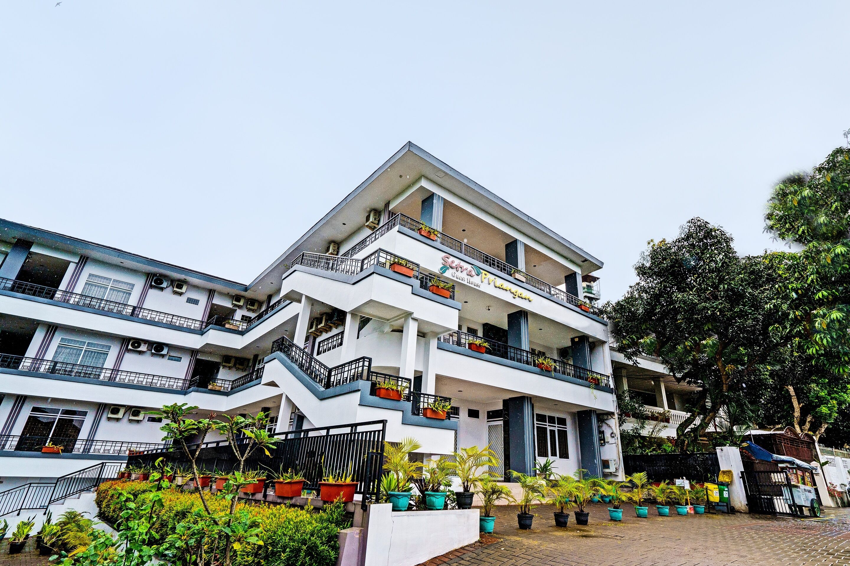 A multi-story hotel with balconies, potted plants, and a paved entrance area.