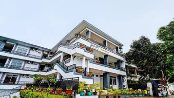 A multi-story hotel with balconies, potted plants, and a paved entrance area.