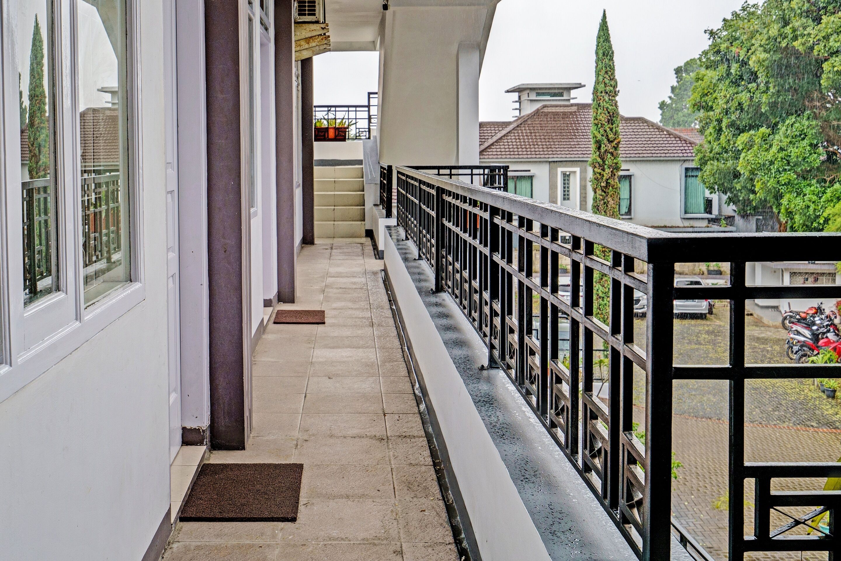A balcony with a black railing, a tiled floor, and a view of a residential area with houses and a parked motorcycle.