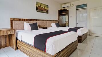 A double bed with a wooden headboard and two bedside tables, a white door, and a painting on the wall.