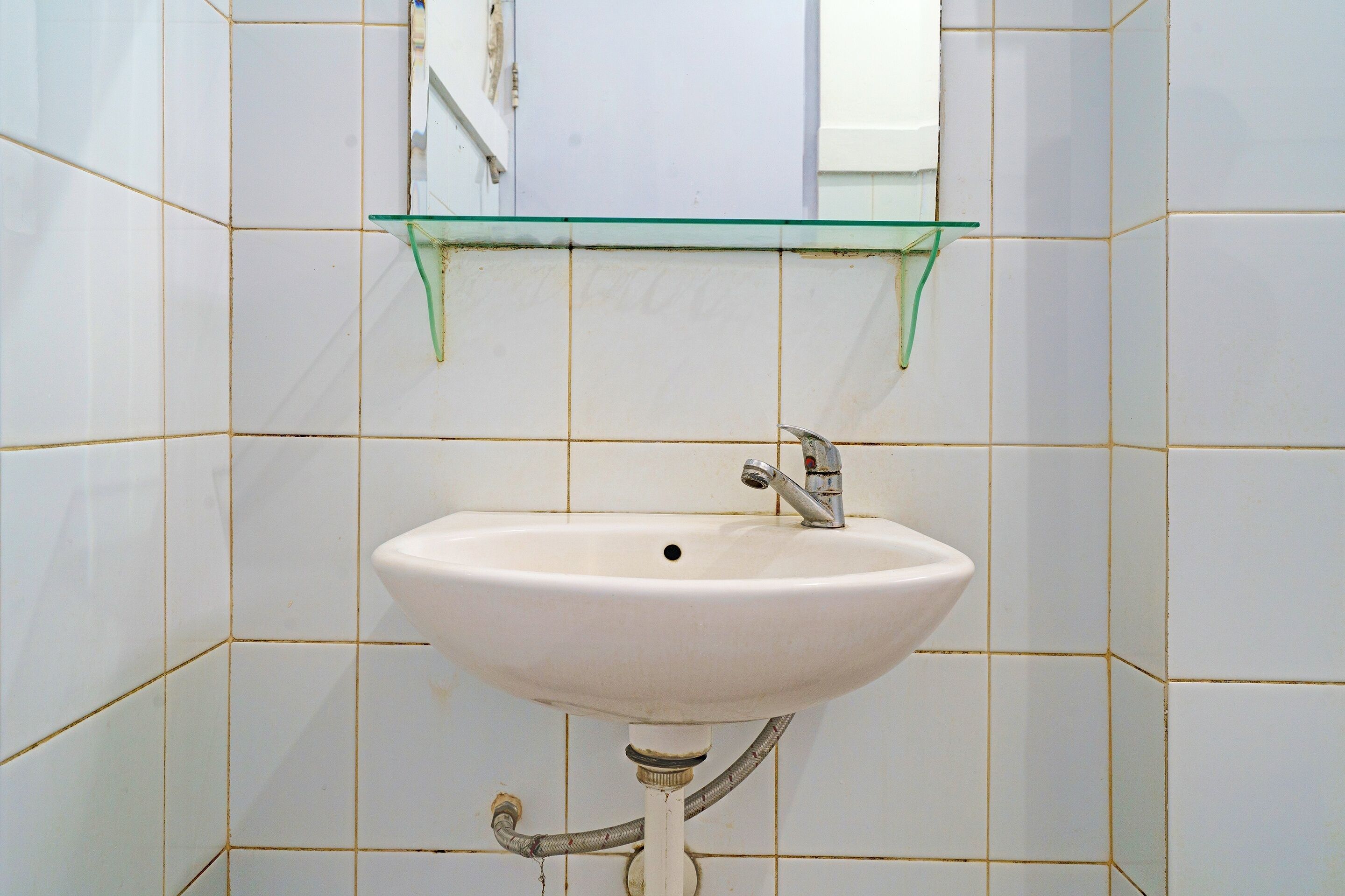 A bathroom with a white sink, a glass shelf above it, and tiled walls.