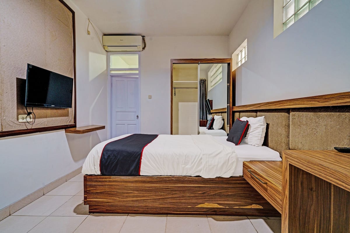 Una habitación de hotel moderna con una cama de madera, un televisor de pantalla plana montado en la pared y un espejo grande sobre la cama.