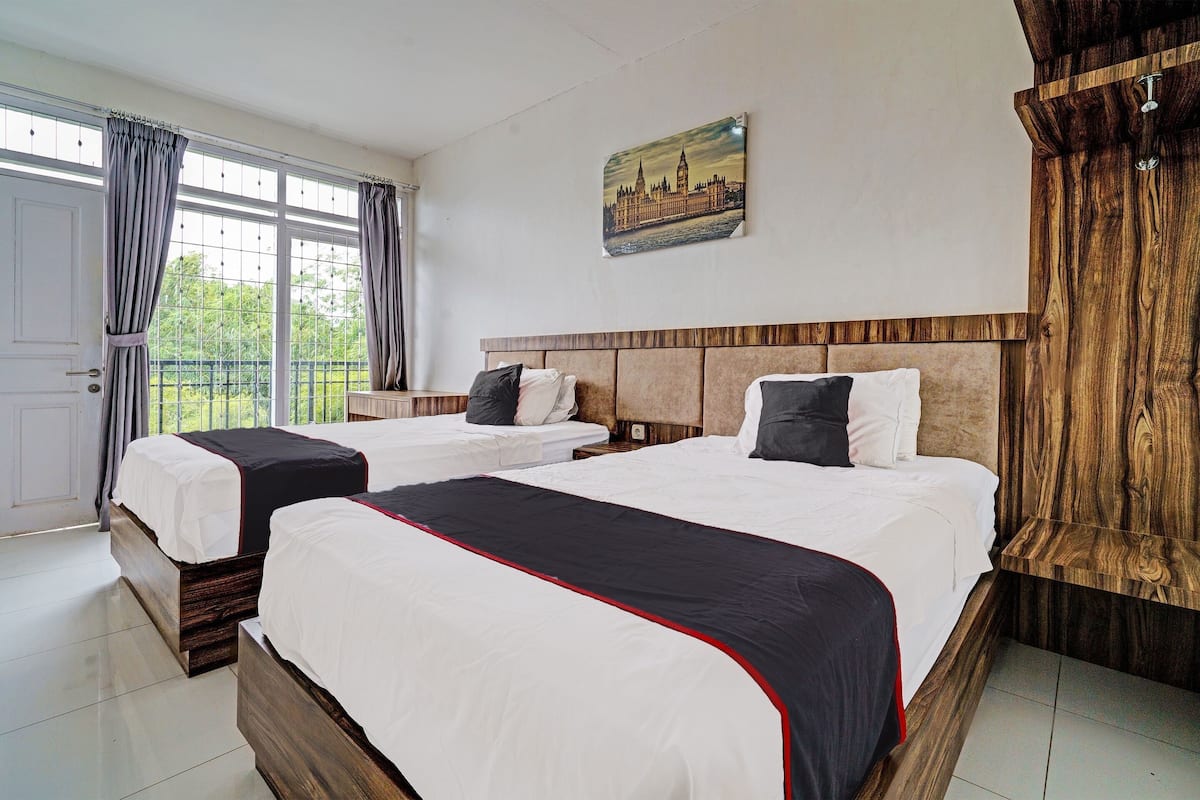 Habitación de hotel con dos camas, un cabecero de madera, una pintura de paisaje urbano y vistas por la ventana.