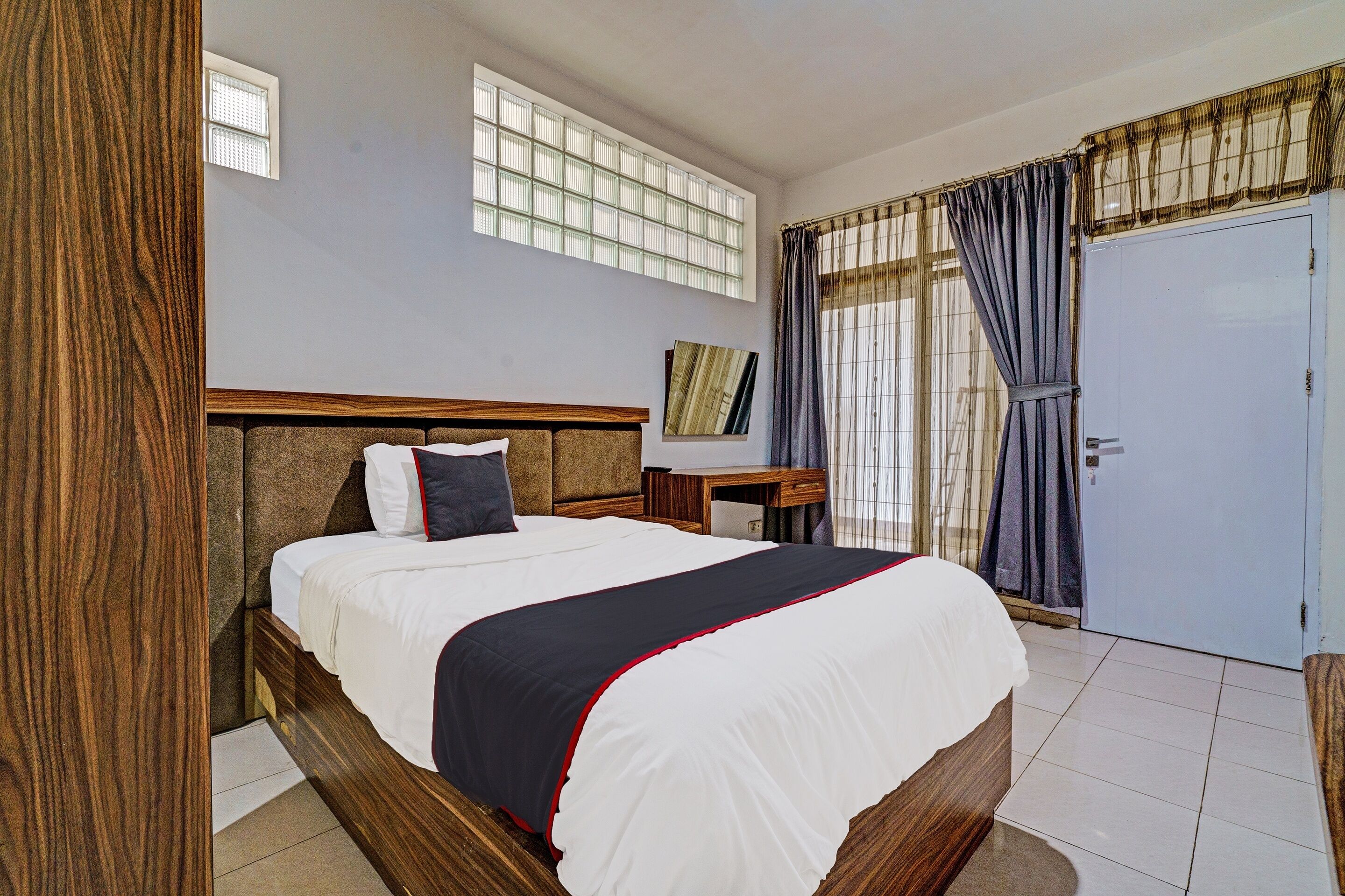 A bedroom with a large bed, a wooden headboard, a nightstand, a desk, and a wardrobe.