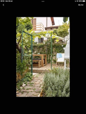 Un jardin agrémenté d’une pergola, d’une terrasse en bois et, au fond, d’un bâtiment blanc.