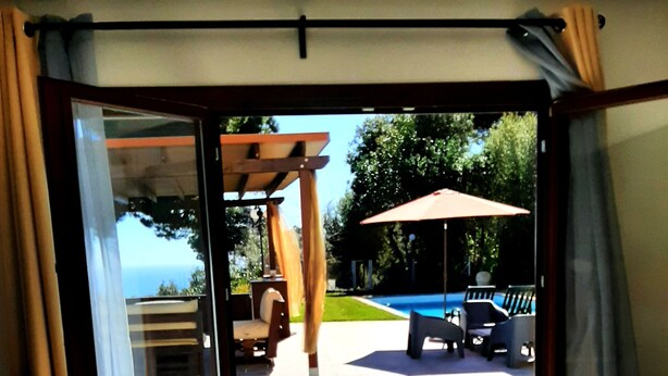 Une pièce dotée d’une porte-fenêtre coulissante donnant sur une terrasse extérieure avec une piscine, des sièges et une pergola.