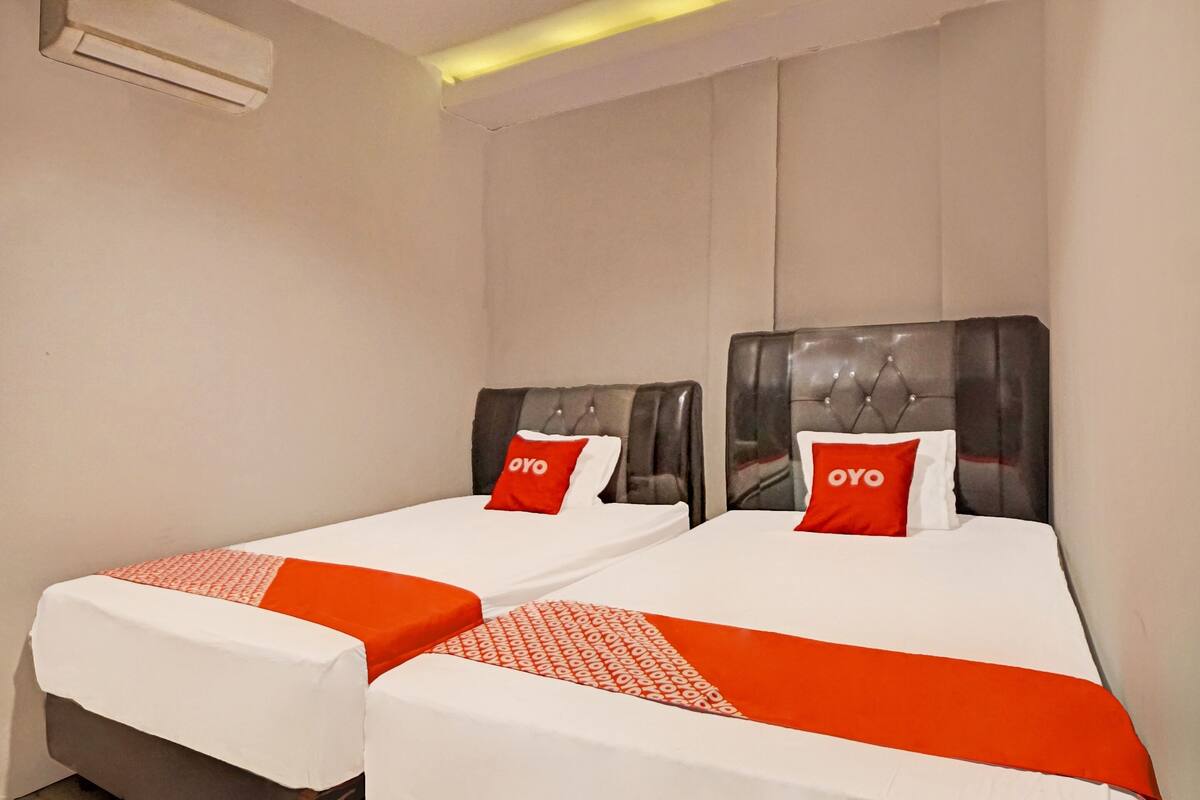 A hotel room with two single beds, each with a headboard and a red pillow with the word "OYO".