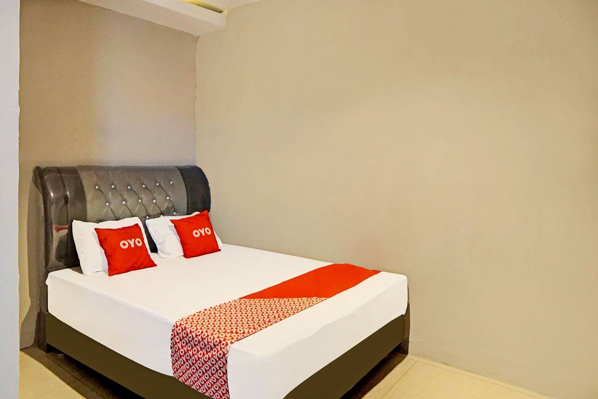 A neatly made bed with a white and red bedspread, two red pillows with the word "OYO" on them, and a grey upholstered headboard.