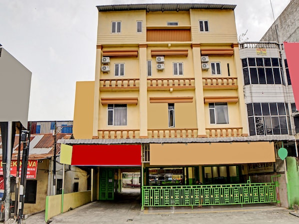 A multi-story building with a flat facade, multiple air conditioning units, and a green metal fence in front.