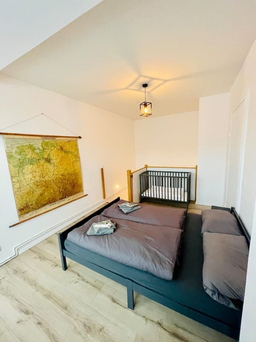 A small, modern room with a bed, a crib, a map on the wall, and a hanging light fixture.