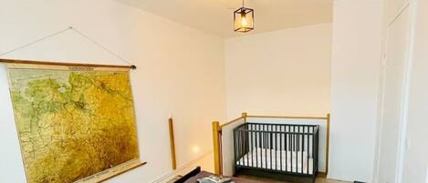 A small, modern room with a bed, a crib, a map on the wall, and a hanging light fixture.