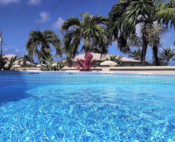 Piscina azul e límpida rodeada por palmeiras e um edifício com telhado vermelho.
