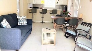Een woonkamer met een bank, stoelen, een eettafel en een keuken op de achtergrond.