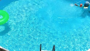 Piscina azul cristalina com um flutuador de argola verde e uma pessoa na água.