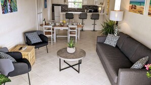 Una sala de estar moderna con un sofá gris, dos sillones, una mesa de centro y un comedor con una mesa y sillas blancas.