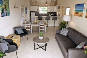 A modern living room with a grey sofa, two armchairs, a coffee table, and a dining area with a white table and chairs.