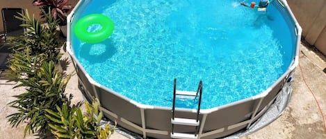 A round above-ground pool with a ladder, surrounded by potted plants.