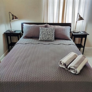 A neatly made bed with a patterned bedspread, two pillows, and two rolled towels. There are two bedside tables with lamps. - Serene escape 2 bedroom with Pool (Oistins)