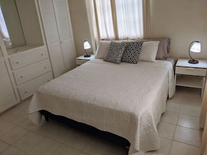 A bedroom with a large bed, two bedside tables, a dresser, and a window with curtains.