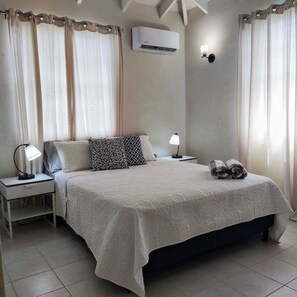 Une chambre à coucher comprenant un lit, deux tables de chevet, un appareil de climatisation et des rideaux.